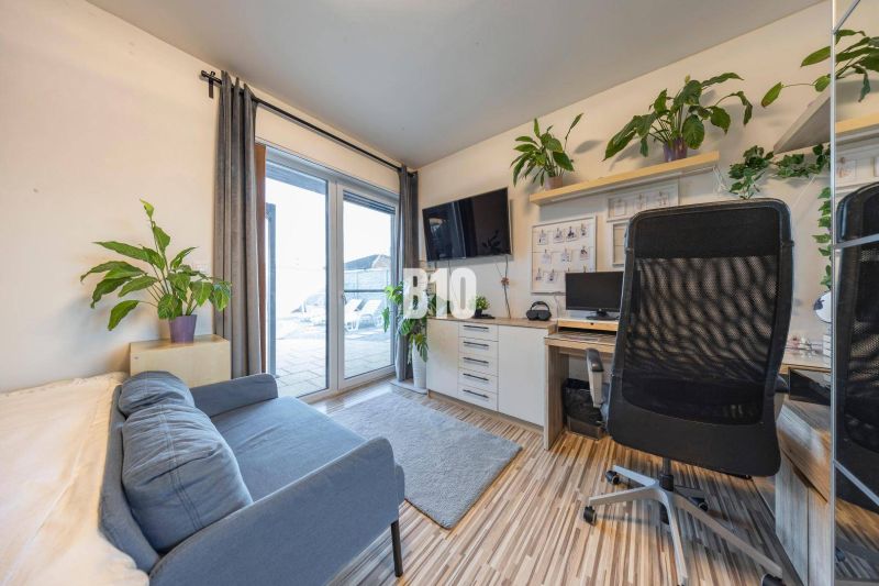 Kanzlei in einem Einfamilienhaus mit Sofa, Schreibtisch, Fernseher und Pflanzen.