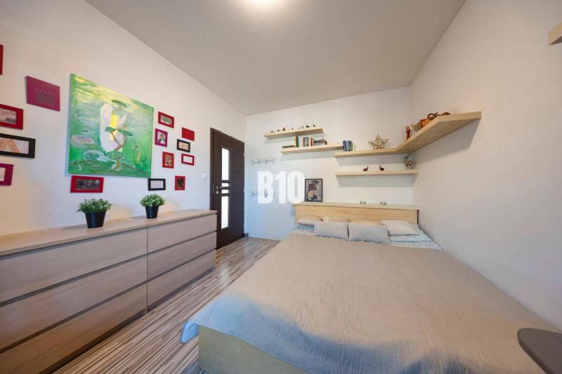 Schlafzimmer in einem Einfamilienhaus mit Bett, Regalen, Bildern und Boden mit Holzdekor.