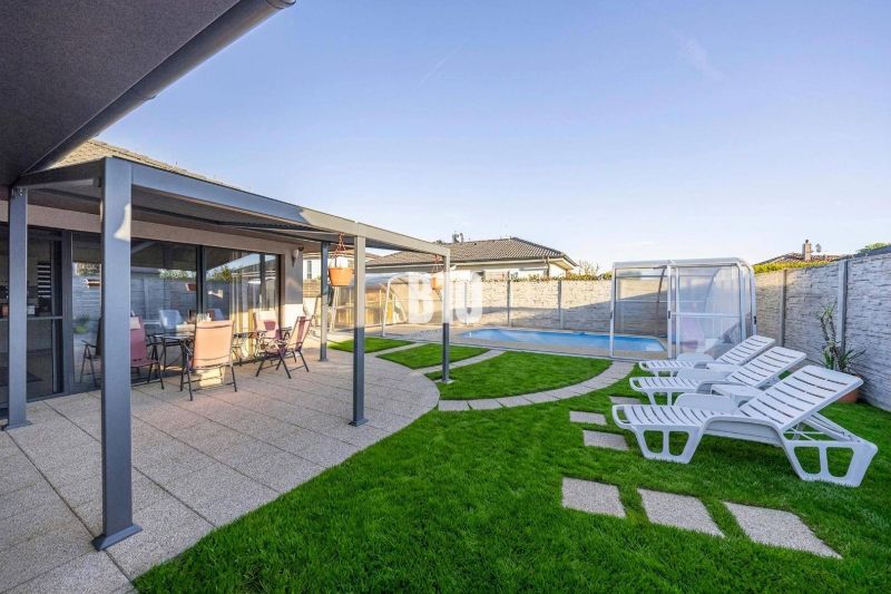 Ein Einfamilienhaus in Most pri Bratislave mit Terrasse, Pool und Liegestühlen auf dem Rasen.