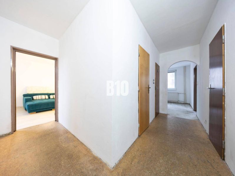 Der Flur in einer 4-Zimmer-Wohnung mit Blick auf das Zimmer mit Sofa, Boden mit Holzdekor.