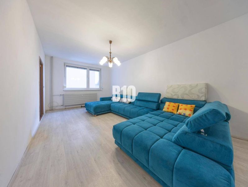 Wohnzimmer in einer Vierzimmerwohnung mit einer türkisfarbenen Couch und einem Boden in Holzoptik.