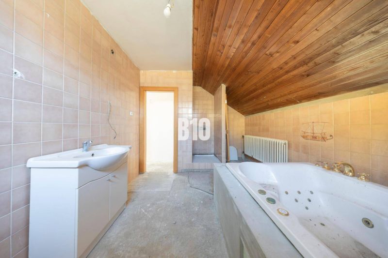 Badezimmer in einem Einfamilienhaus mit Badewanne, Fliesen und Holzdecke.