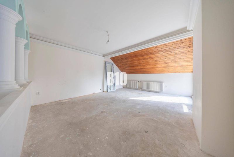 Ein unmöbliertes Zimmer mit einem Heizkörper und einer Holzdecke im Dachgeschoss eines Einfamilienhauses.