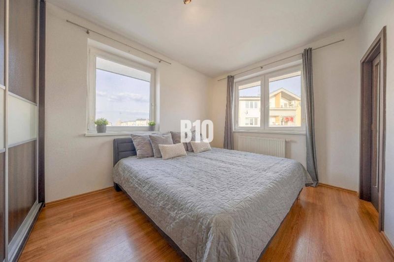 Helles Schlafzimmer mit Bett, großen Fenstern und Holzboden in einer 2-Zimmer-Wohnung.