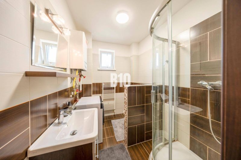 Badezimmer in einer 2-Zimmer-Wohnung mit dunklen Fliesen und Duschkabine.