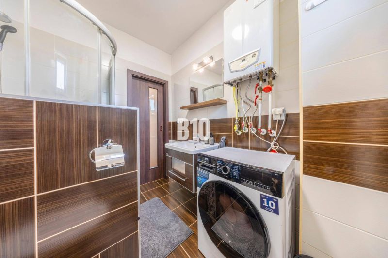 Badezimmer mit Waschmaschine und Duschkabine in einer 2-Zimmer-Wohnung mit Holzboden.
