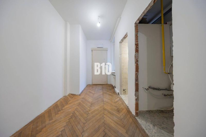 Der Flur in der 3-Zimmer-Wohnung mit einem Boden in Holzoptik und einem Rohr in der Wand.