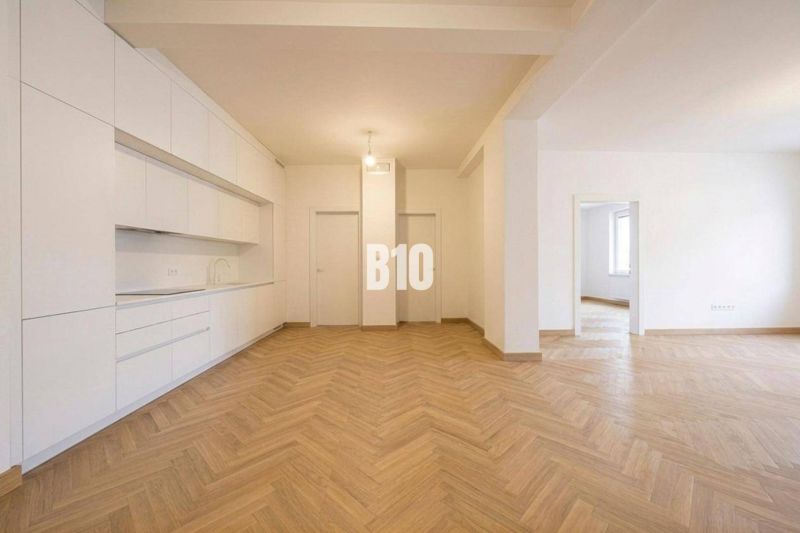 Innenraum einer 3-Zimmer-Wohnung mit weißer Küche und Boden in Holzoptik.