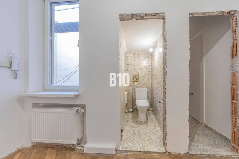 Badezimmer mit Keramikfliesen und Fenster, daneben ein Boden mit Holzdekor.