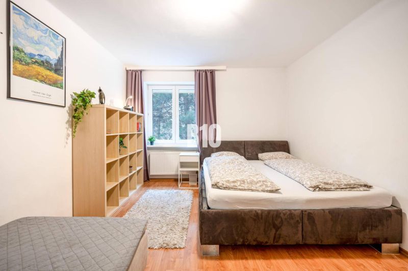 Schlafzimmer in einer 2-Zimmer-Wohnung mit Bett, Regal, Fenster und Boden in Holzoptik.