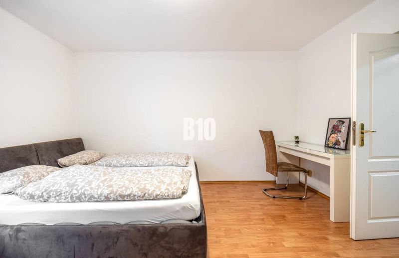 Schlafzimmer in einer 2-Zimmer-Wohnung mit Bett, Tisch und Boden in Holzoptik.