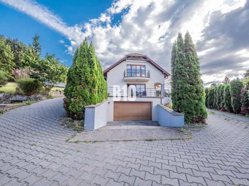 Einfamilienhaus in Marianka mit Strauchumrandung, Garage und teilweise bewölktem Himmel.