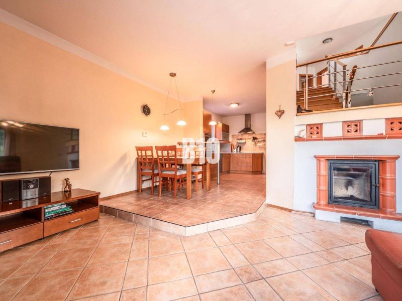 Wohnzimmer eines Einfamilienhauses mit Kamin, Esstisch und Küche mit Fliesenboden.