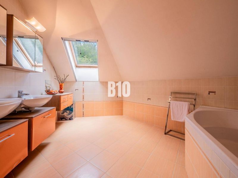 Ein Raum in einem Einfamilienhaus mit zwei Waschbecken, einer Badewanne, einem Dachfenster und orangenen Details.
