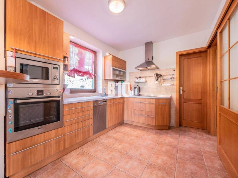 Eine Küche in einem Einfamilienhaus mit Fliesenboden, Holzelementen und Edelstahlgeräten.