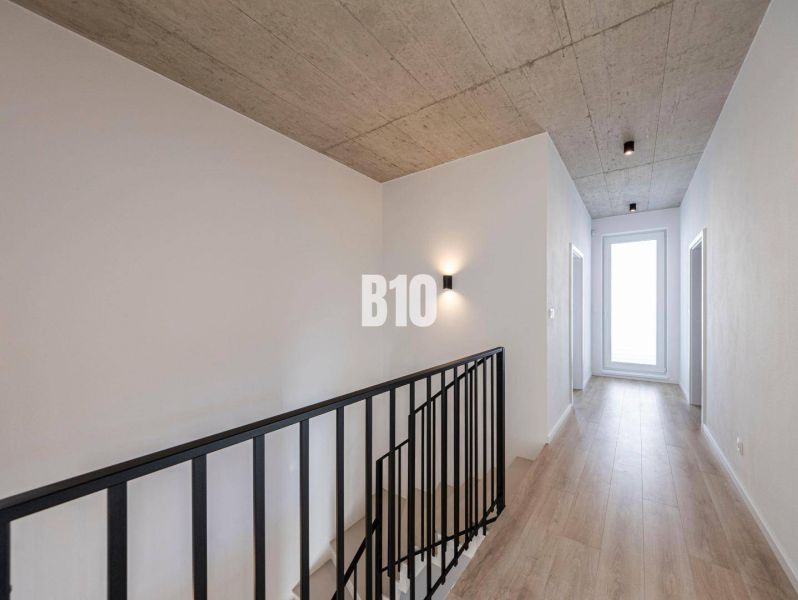 Ein Flur mit Betondecke, Holzboden und Treppe in einem Einfamilienhaus.