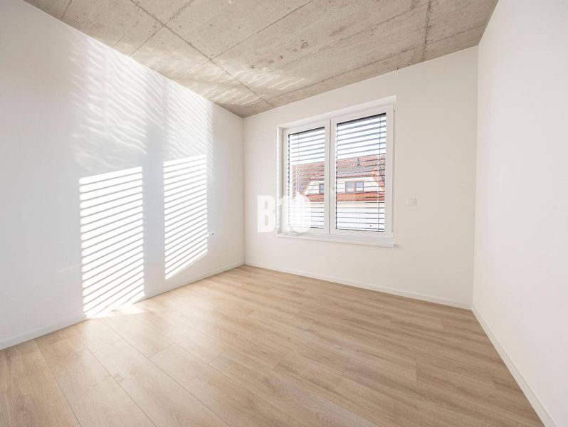 Ein heller Raum mit Holzboden in einem Einfamilienhaus, mit einem großen Fenster und weißen Wänden.