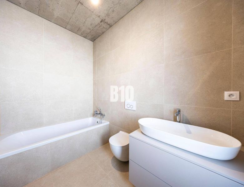 Badezimmer mit gefliester Badewanne in einem Einfamilienhaus. Decke aus Beton.