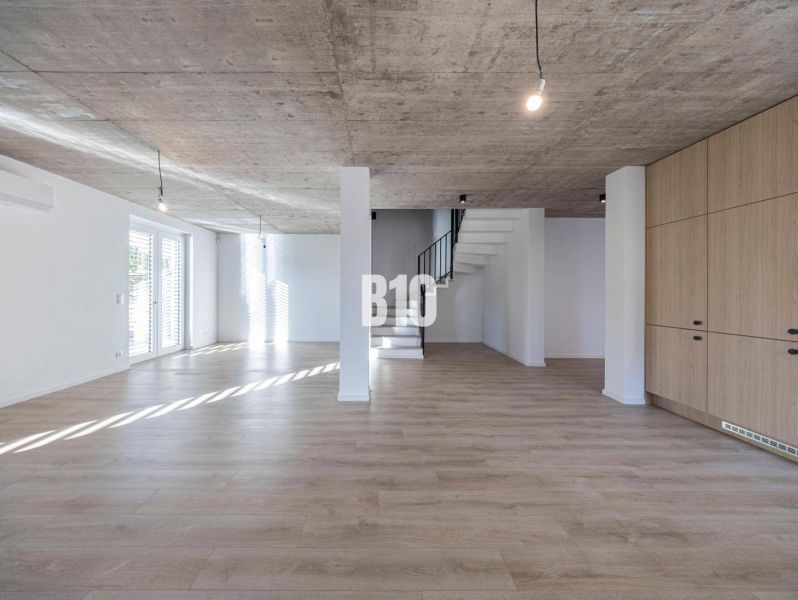 Ein Einfamilienhaus mit einem Boden in Holzoptik und einer Betondecke, Treppen und großen Fenstern.