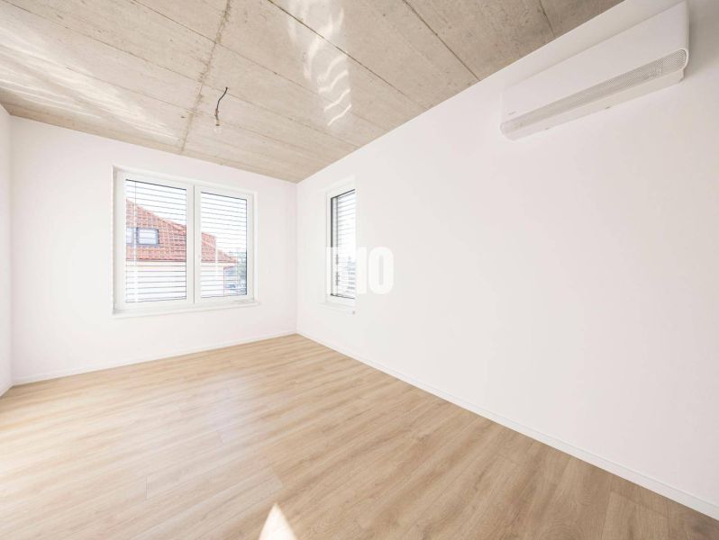 Ein Zimmer in einem Einfamilienhaus mit einem Boden in Holzoptik und großen Fenstern.