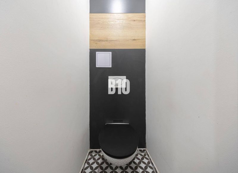 Toilette mit schwarzem Sitz und geometrischem Boden in einer 3-Zimmer-Wohnung.