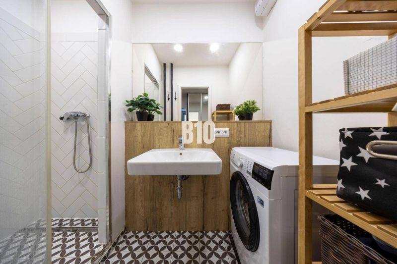 Das Badezimmer in der 3-Zimmer-Wohnung enthält eine Dusche, ein Waschbecken, eine Waschmaschine und ein Holzregal.