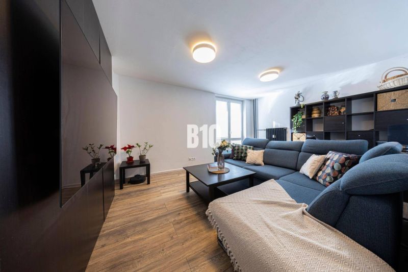 Wohnzimmer in einer 3-Zimmer-Wohnung mit einem blauen Sofa und einem Boden in Holzoptik.