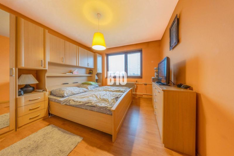 Ein Schlafzimmer in einem Einfamilienhaus mit orangefarbenen Wänden und einem Boden in Holzoptik.