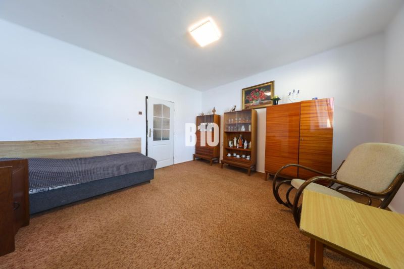 Ein Zimmer in einem Einfamilienhaus mit einem Sofa, Schränken und einem Sessel auf dem Teppich.