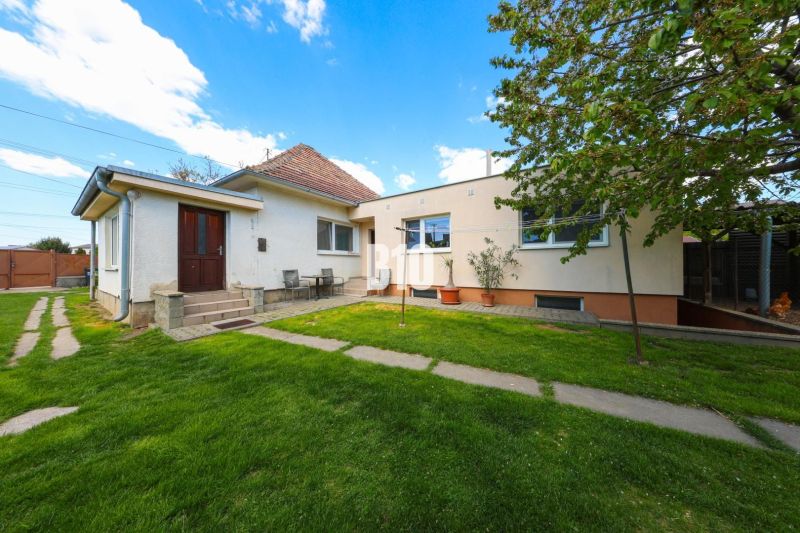 Ein Einfamilienhaus in Kalinkovo mit einem gepflegten Garten und zwei Eingängen unter blauem Himmel.