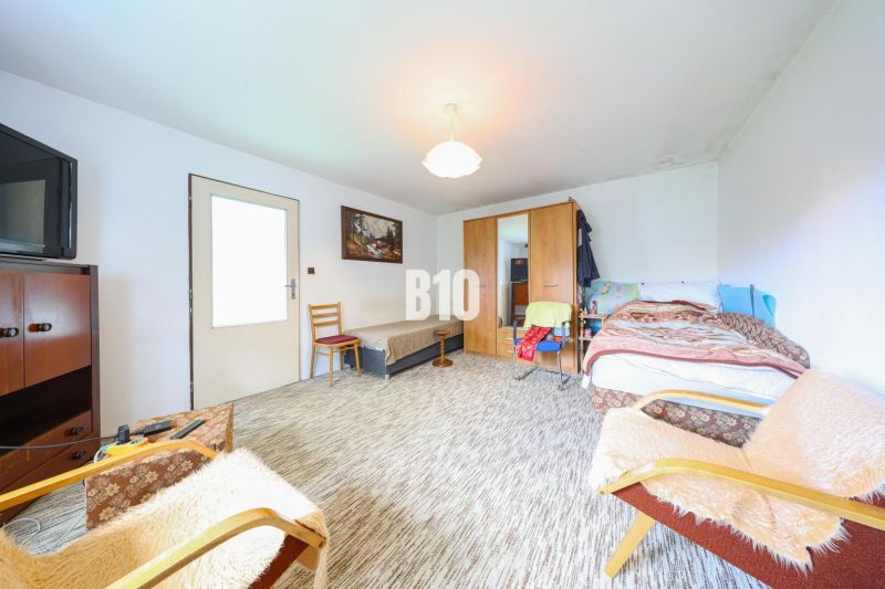 Ein Zimmer mit Bett, Schränken und Sessel in einem Einfamilienhaus. Ein Teppich bedeckt den Boden.