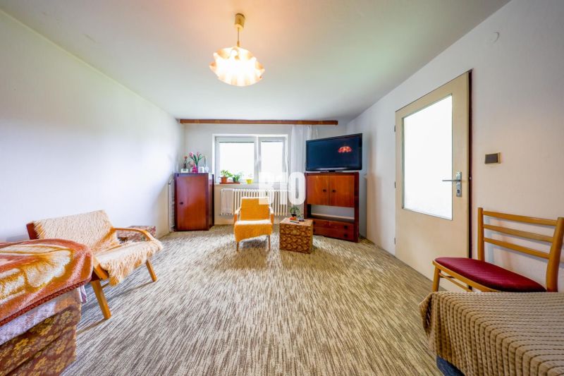 Wohnzimmer in einem Einfamilienhaus mit Teppichboden und einfacher Einrichtung.