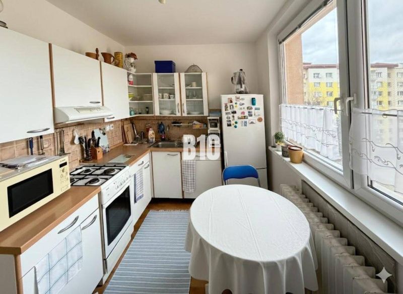 Küche in einer 3-Zimmer-Wohnung mit Tisch, Kühlschrank und Küchenzeile mit Spüle.