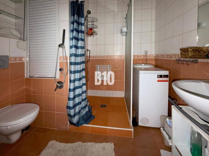 Badezimmer in einer 3-Zimmer-Wohnung mit orangefarbenen Fliesen, Dusche, Waschmaschine und WC.