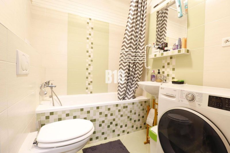 Badezimmer in einer 2-Zimmer-Wohnung mit grünen Fliesen, Waschmaschine und Badewanne.