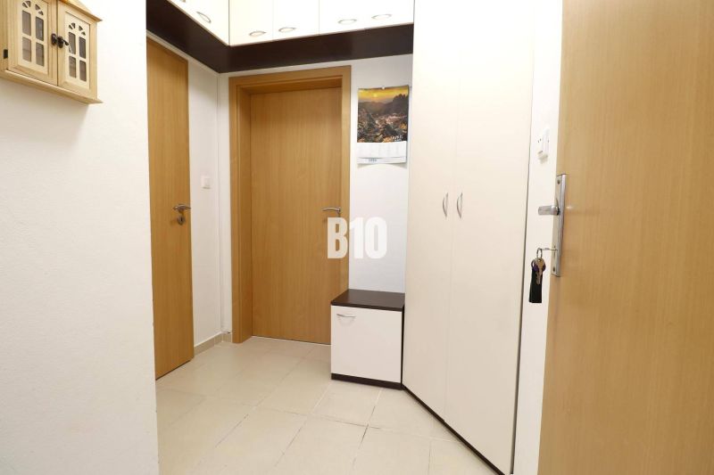 Eingangsbereich in einer 2-Zimmer-Wohnung mit weißen Möbeln und beigefarbenen Fliesen.