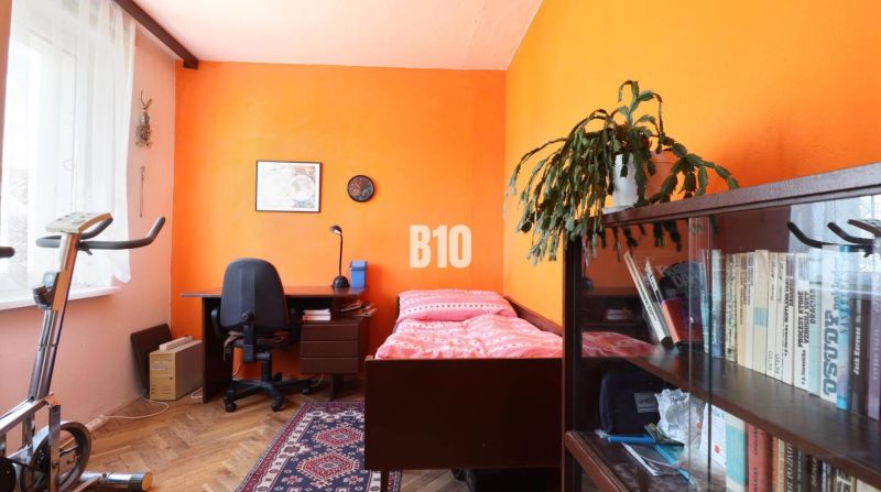 Zimmer in einer 3-Zimmer-Wohnung mit Ausstattung: Bett, Tisch, Regal und Heimtrainer.