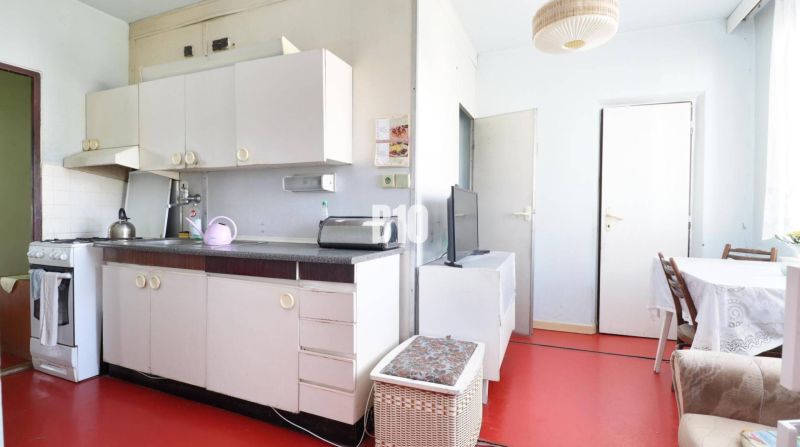 Küche in einer 3-Zimmer-Wohnung mit weißen Möbeln und rotem Boden.