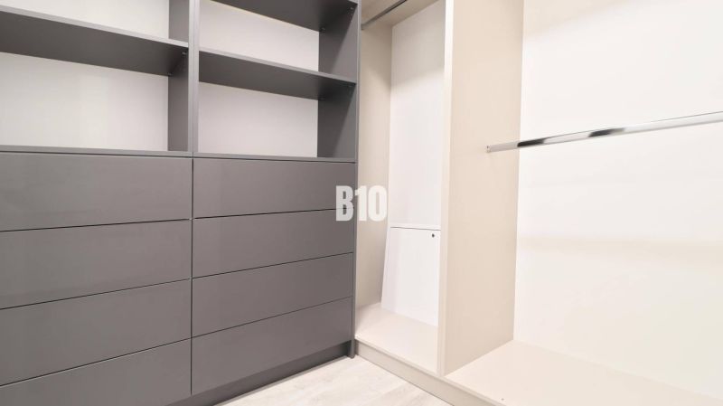 Ein Kleiderschrank mit grauen Schränken und einer Kleiderstange in einer Zweizimmerwohnung.