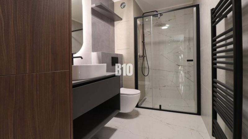 Badezimmer in einer 2-Zimmer-Wohnung mit rahmenloser Dusche und Waschbecken auf Holzdekor.
