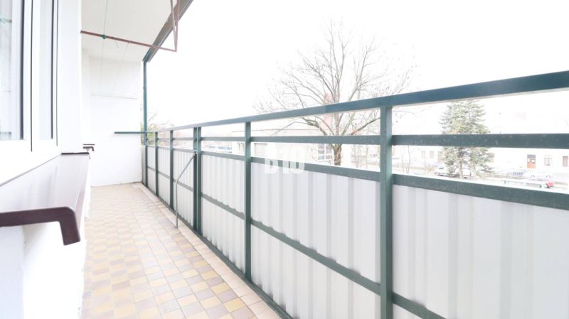 Balkon einer 3-Zimmer-Wohnung mit Blick auf Bäume und Fliesen.