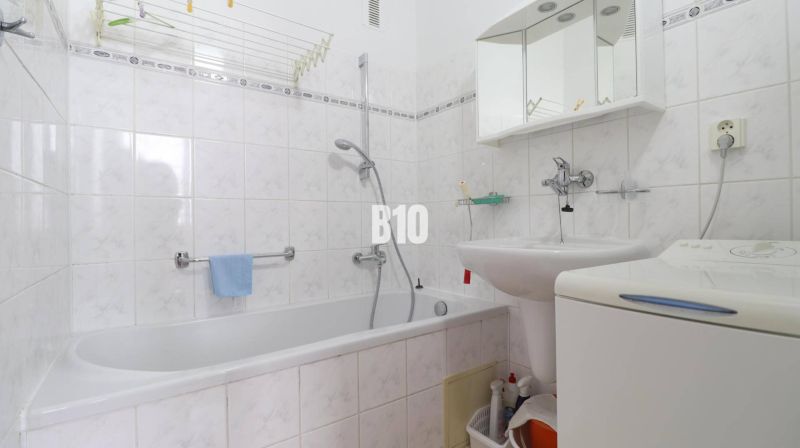 Badezimmer in einer 3-Zimmer-Wohnung mit Badewanne, Waschbecken, Spiegel und Waschmaschine.