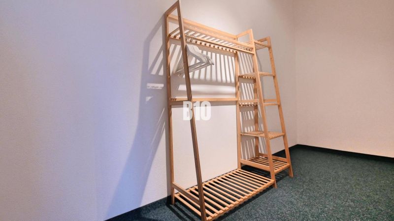 Ein Holzständer mit Kleiderbügeln in einer 3-Zimmer-Wohnung auf einem dunklen Teppich.