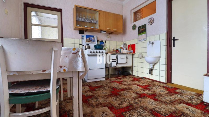 Eine Küche in einem Einfamilienhaus mit einem Kachelherd und einem rotbraunen Teppich.