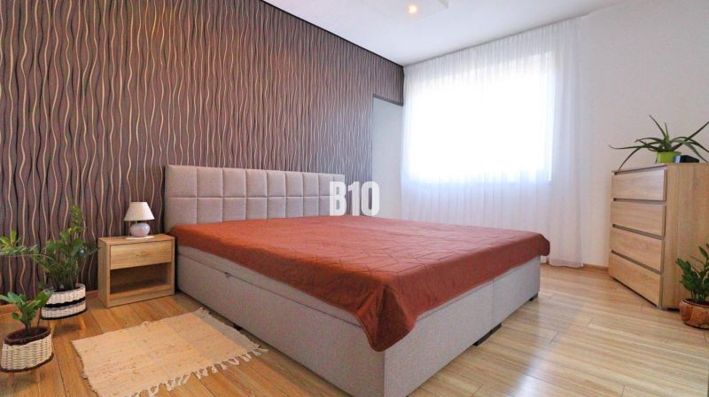Schlafzimmer mit Bett, Tapetenwand, Holzdekorboden und Möbeln in einem Einfamilienhaus.