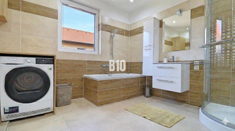 Ein Badezimmer in einem Einfamilienhaus mit Badewanne, Dusche und Waschmaschine, Boden mit Holzdekor.