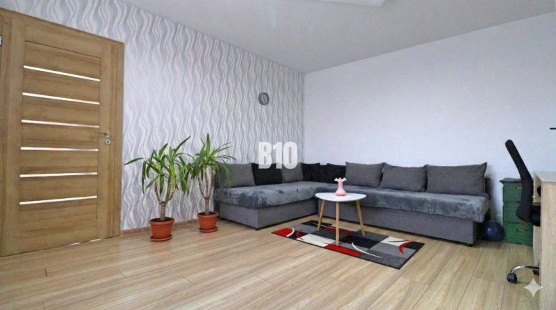 Ein stilvolles Wohnzimmer in einem Einfamilienhaus mit einem Sofa, Pflanzen und einem Boden in Holzoptik.
