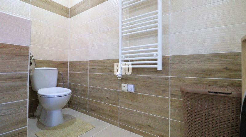 Badezimmer mit Toilette, Fliesen mit Holzdekor, Heizkörper, Korb, Boden mit Holzdekor.