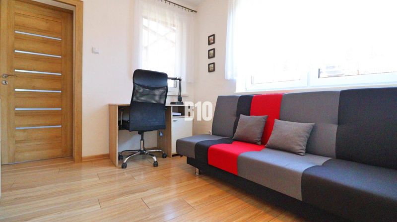 Ein Zimmer eines Einfamilienhauses mit einem Schreibtisch, einem Stuhl und einem bunten Sofa, Boden mit Holzdekor.