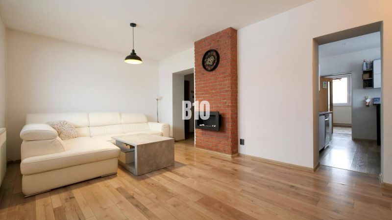 Wohnzimmer in einer 3-Zimmer-Wohnung mit weißem Sofa, Ziegelwand und Holzboden.